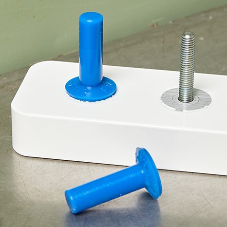Valge plastdetail metallpoldi ja siniste plastmutritega tööstuslikul metalllaual