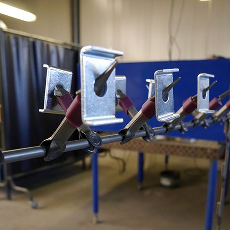 Metallklambrid ripuvad punastel pihikutel pulbervärvimise konveieriliini varrastel tööstushallis