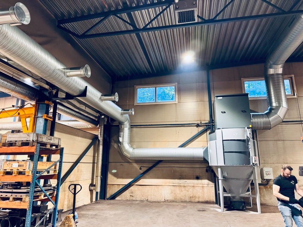Tööstuslik tolmueraldusseade ja ventilatsioonitorustik laohoones, taustal töötaja