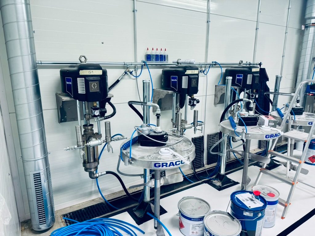Kolm Graco Dura-Flo tööstuslikku värvipumpa seinal koos õhuvoolikute ja värvinõudega maalitöökojas