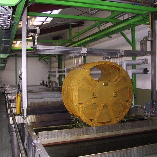 Suured kollased metalldetailid kastetakse tööstuslikus eeltöötlusvannis pinnakatte protsessiks