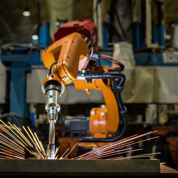 Oranž tööstusrobot teostab keevitust metallil, tekitades sädemeid tehase töökojas