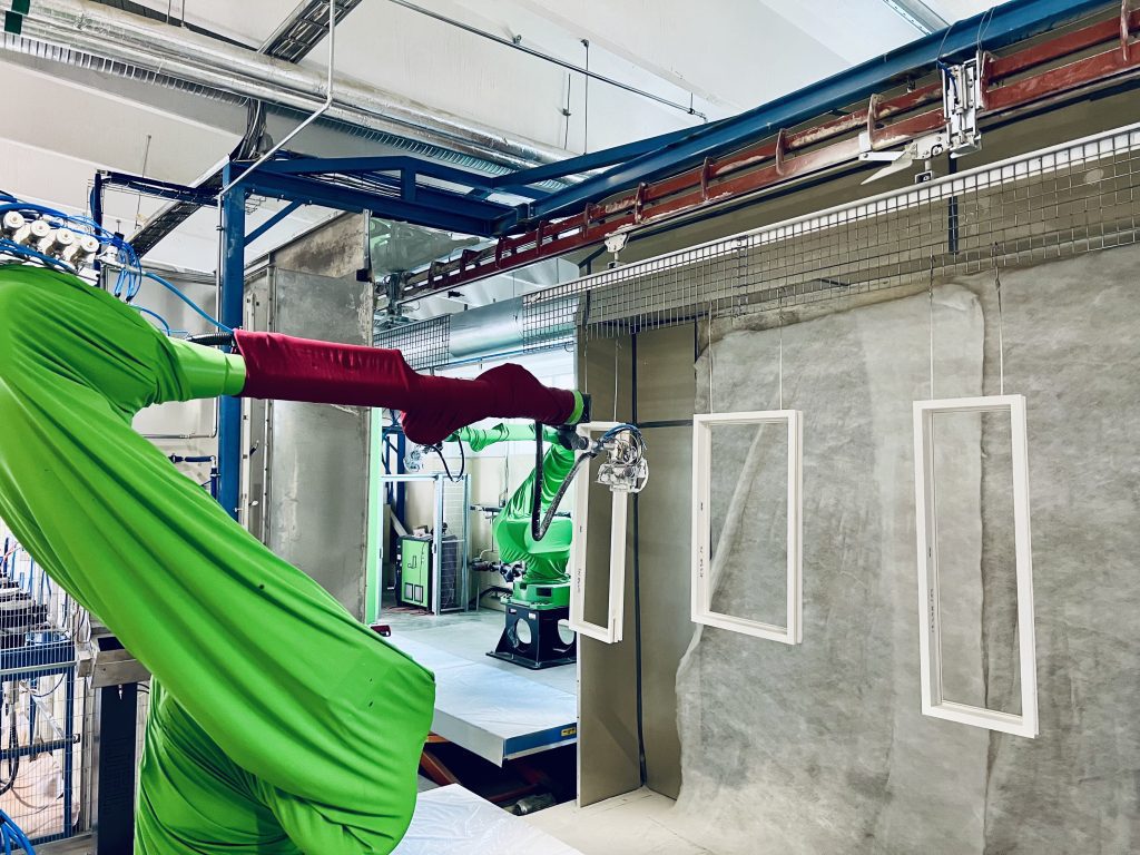 Roheline ja punane tööstusrobot värvib pulbervärviga aknaraame automatiseeritud värvimiskabiinis