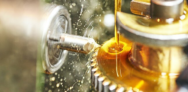 Kuldne määrdeõli voolab metalltööstusseadme hammasrattale automaatse õlitussüsteemi töö käigus